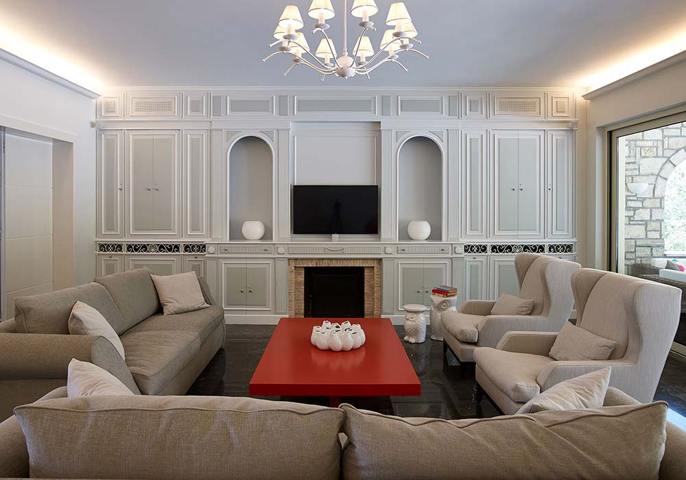The Villa Alpha living room, panelled white walls, a fireplace and pale sofas around a red table