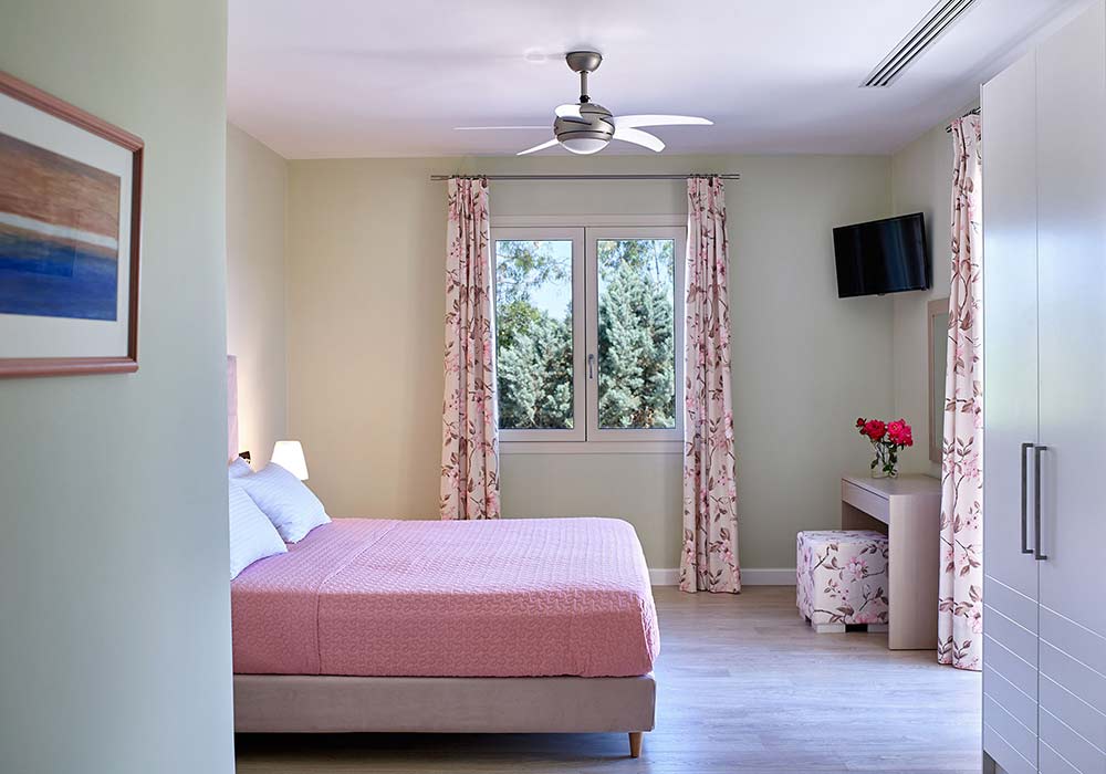A Villa Alpha bedroom in pink with floral curtains and a window onto the garden